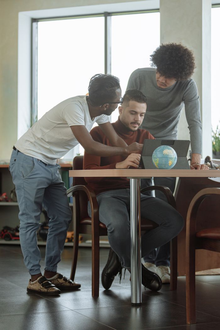 About Three young adults collaborating in a modern office setting, engaged over a laptop.