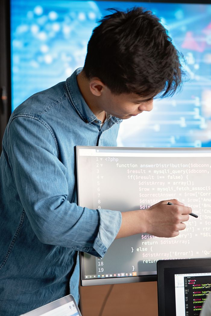 Menu Asian male programmer writing code on a computer monitor in an office setting.